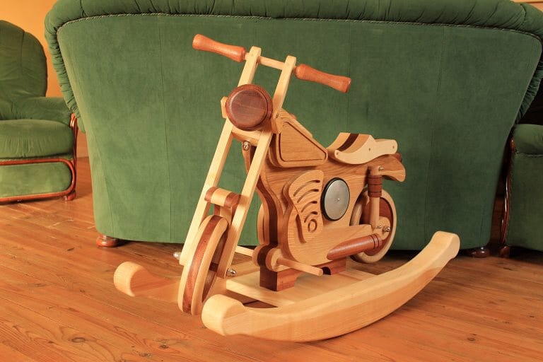 Cheval à bascule moto en bois artisanal clair et foncé, posé sur un parquet devant un canapé vert.