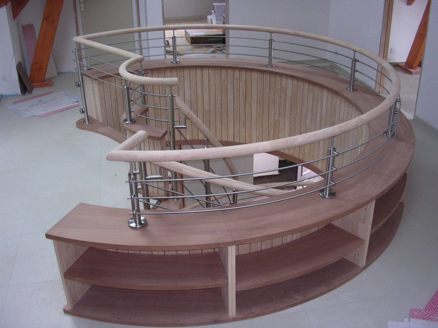 Escalier demi-lune en bois avec garde-corps moderne en inox et câbles horizontaux, finition étagères intégrées.