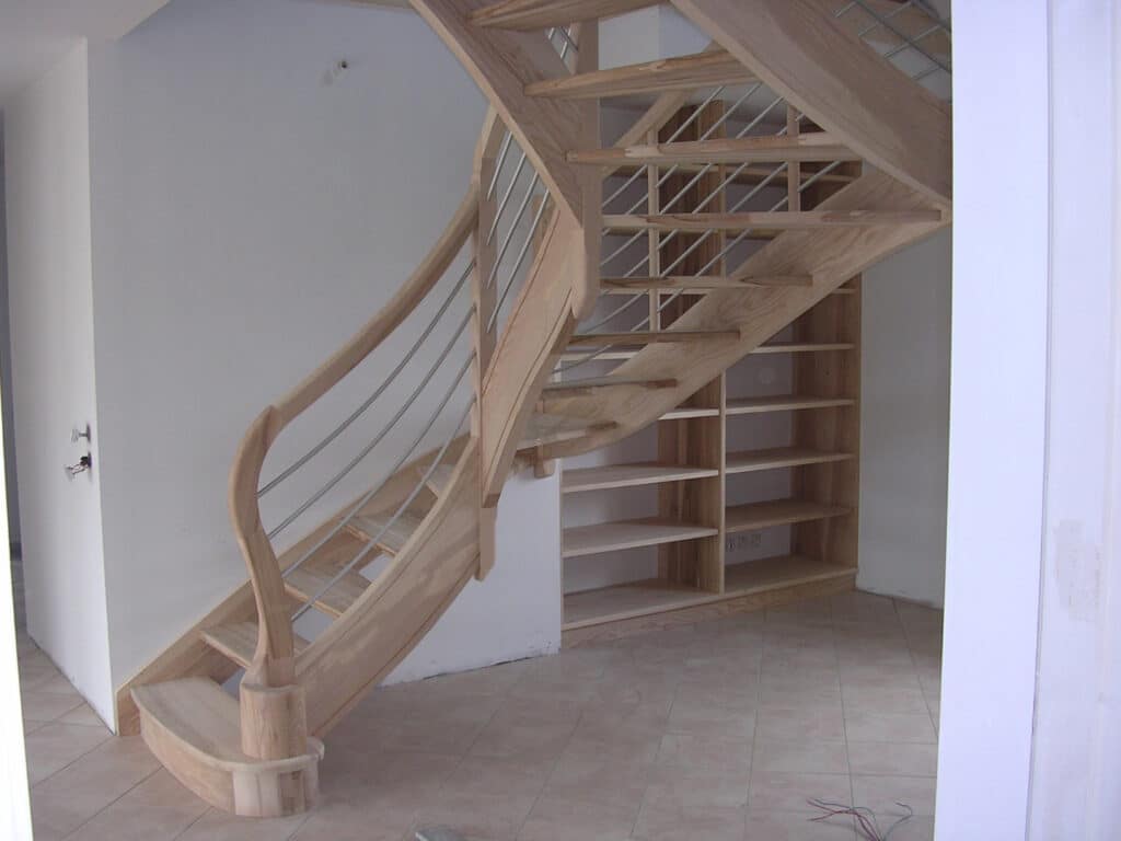 Escalier droit en bois clair avec garde-corps à lisses métalliques horizontales, intégrant des étagères sous-pente.