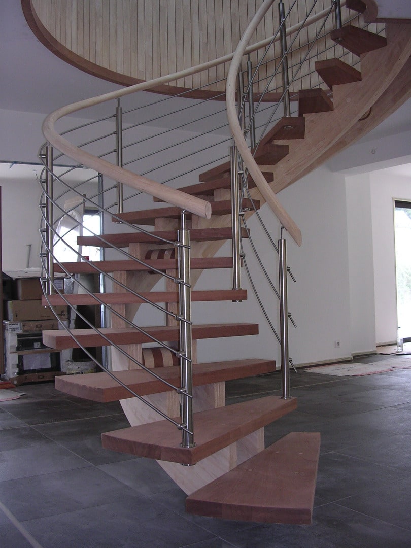 Escalier hélicoïdal moderne avec marches en bois rouge, balustrade en inox et main courante courbe en bois clair.