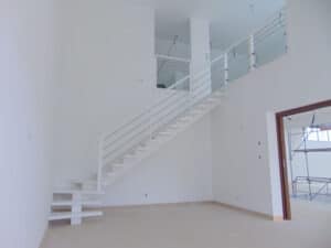 Escalier flottant blanc moderne à limonnette, avec garde-corps à câbles métalliques et panneaux de verre, dans un intérieur en construction.