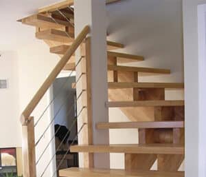 Escalier flottant moderne en bois clair avec poteaux verticaux et câbles métalliques fins formant la rampe.