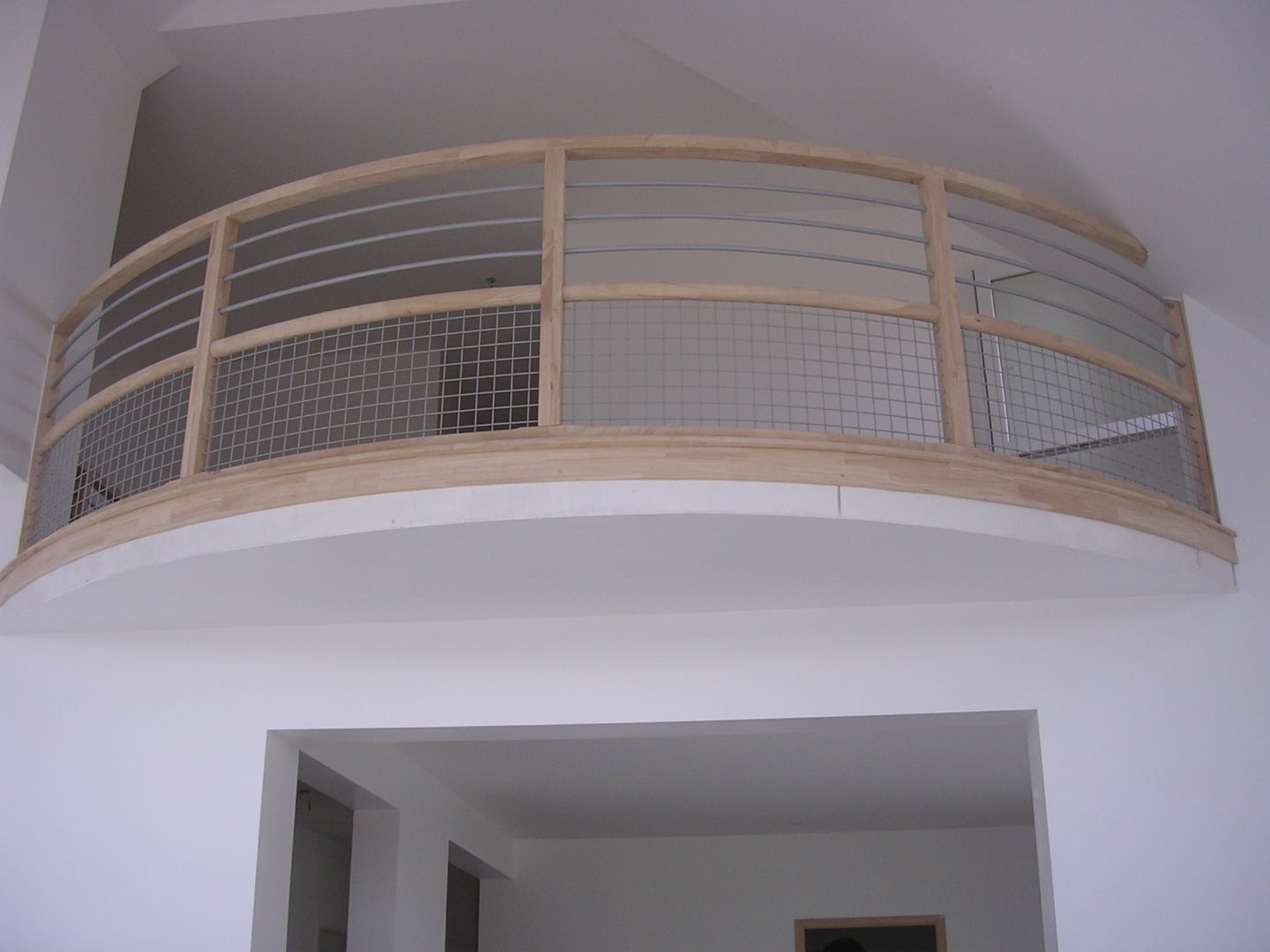 Balcon intérieur incurvé avec garde-corps moderne combinant bois clair, câbles horizontaux en métal et panneaux grillagés.