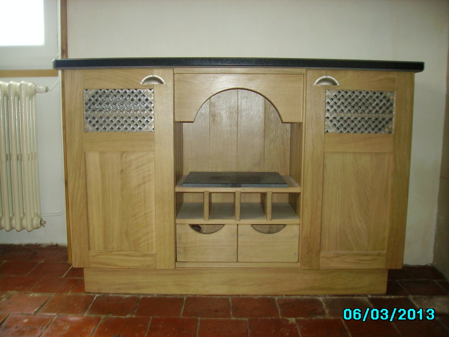 Meuble en bois clair de style rustique avec dessus noir, tiroirs et portes à grille métallique. Date : 06/03/2013.