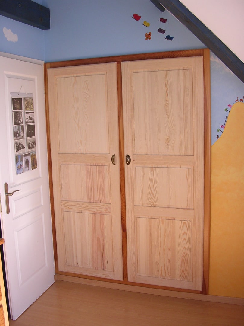 Plaque de placards en pin clair à deux portes dans une chambre mansardée bleu ciel avec décorations papillons et porte blanche ouverte.