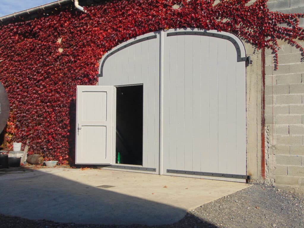 Porte de grange grise et vigne vierge rouge d'automne Grande porte de grange grise à deux vantaux avec une petite porte ouverte, devant un mur couvert de vigne vierge rouge flamboyant.