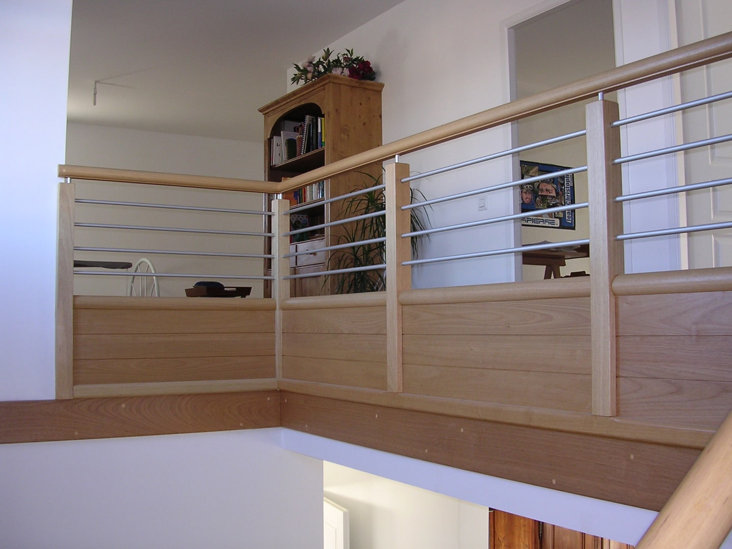 Rambarde d'étage en bois clair et métal brossé, avec bibliothèque en bois et affiche murale 'APIERRE' visible à l'étage.