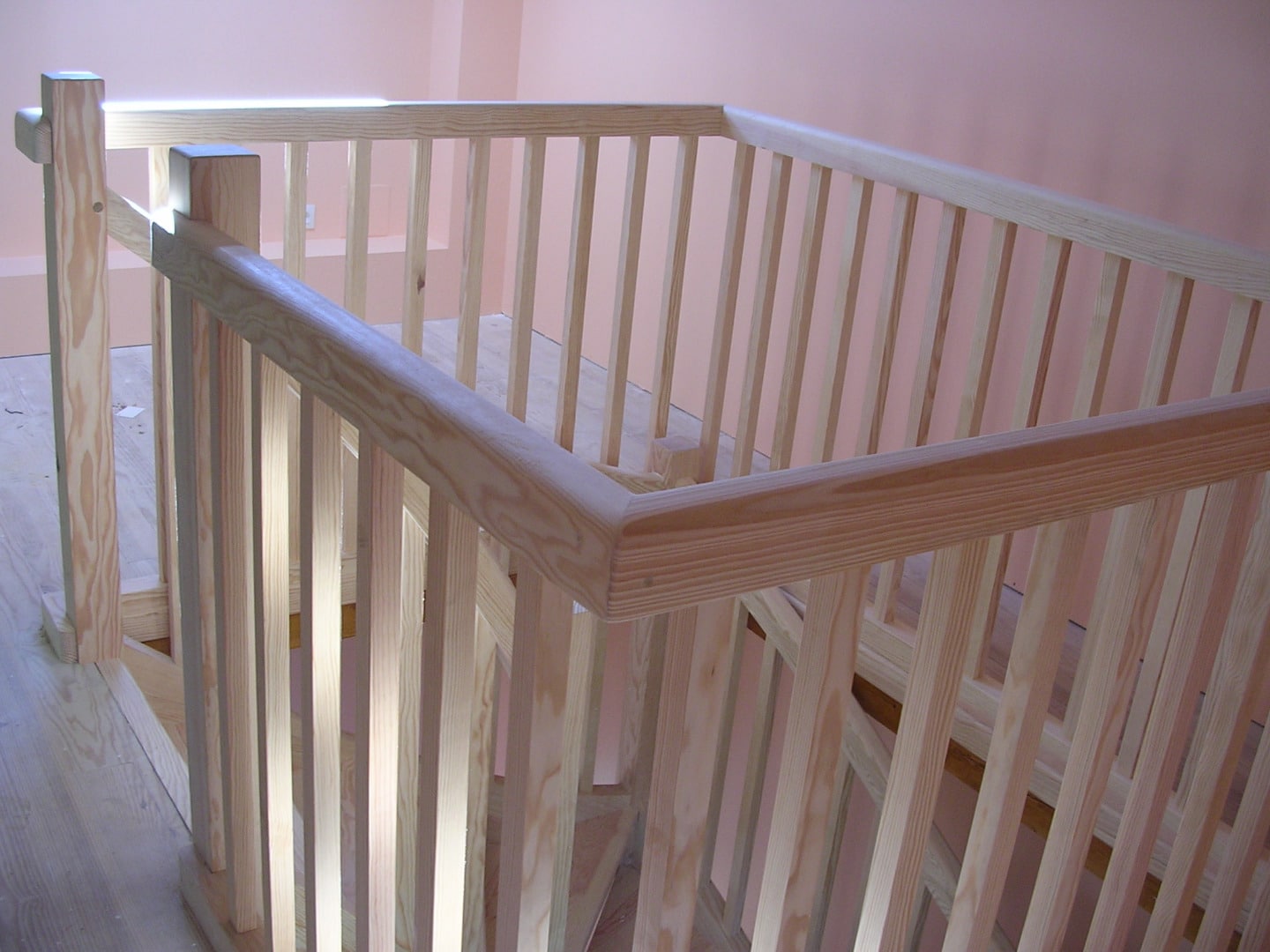 Rambarde et balustrade d'escalier neuves en bois clair, style contemporain, contre un mur rose pâle.