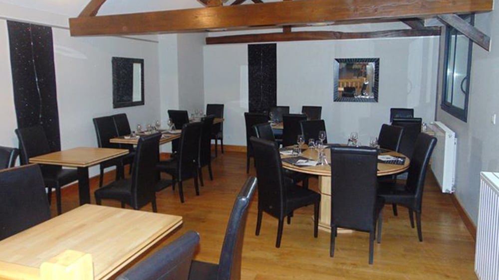 Restaurant Chic : Tables Bois, Chaises Cuir Noir Salle de restaurant élégante avec tables en bois clair, chaises noires en cuir, et poutres apparentes au plafond. Ambiance chaleureuse.