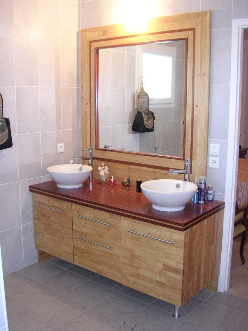 Salle de bain moderne avec meuble vasque double en bois clair, vasques rondes blanches, comptoir rouge bordeaux et grand miroir encadré.