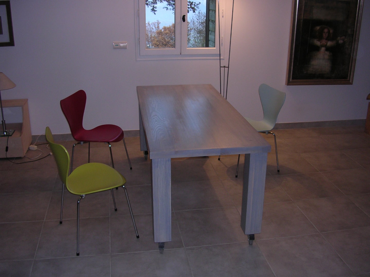 Salle à manger moderne avec table grise à roulettes et trois chaises Arne Jacobsen : une rouge, une jaune-vert et une vert pâle.